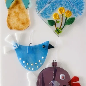 A collection of colorful, whimsical glass art pieces featuring a flip-flop, a bird, a fish, and a whimsical round a heart, made at the Glass Duchess Studio in Port Charlotte, FL