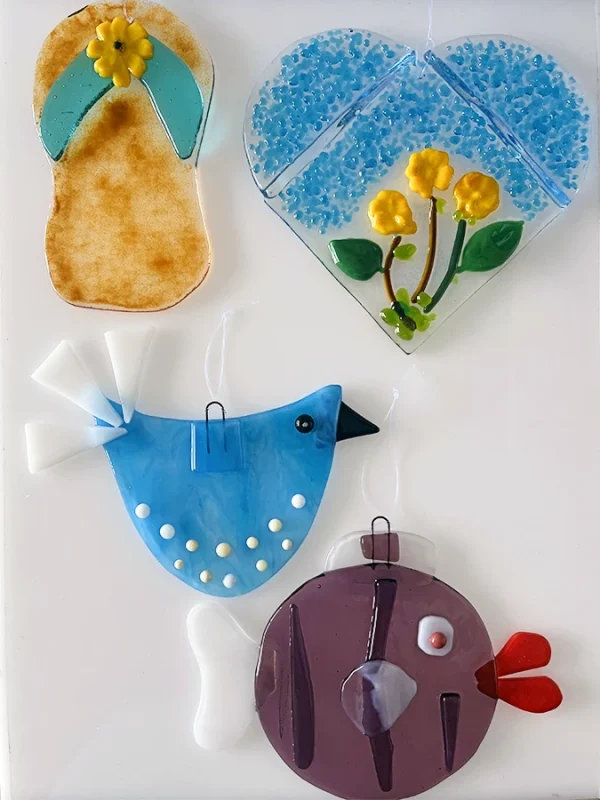 A collection of colorful, whimsical glass art pieces featuring a flip-flop, a bird, a fish, and a whimsical round a heart, made at the Glass Duchess Studio in Port Charlotte, FL
