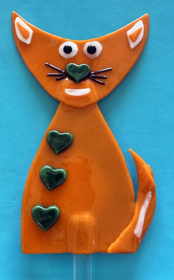 A whimsical ceramic orange cat garden stake with heart accents and playful features on a blue background.