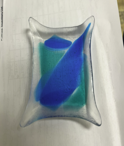 A fused glass art piece with blue and green abstract shapes in a rectangular form.