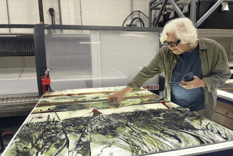An artist examines a large nature-themed painting in a studio.