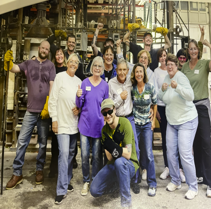 A diverse group of people posing happily in a workshop or factory setting.